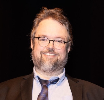 Smiling Caucasian male with glasses and beard, wearing a suit and tie
