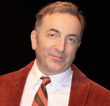 Caucasian male with short hair wearing a red corduroy suit jacket and stripped tie 