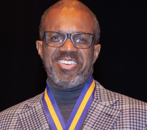 Smiling African American male with thick rimmed glasses in a plaid suit jacket